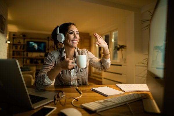features vonage residential plans voip service woman video chat on computer with headphones and coffee mug in hand waving happy smiling